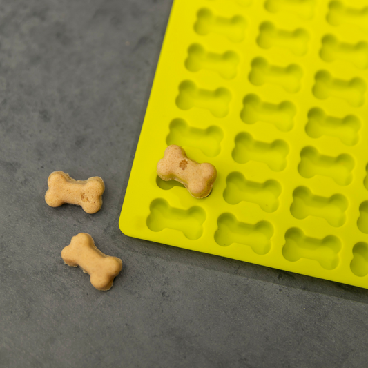 Selbstgebackene Hundeleckerlis in Knochenform neben gelber Silikon Backmatte für Hundekekse, frisch gebacken und natürlich.