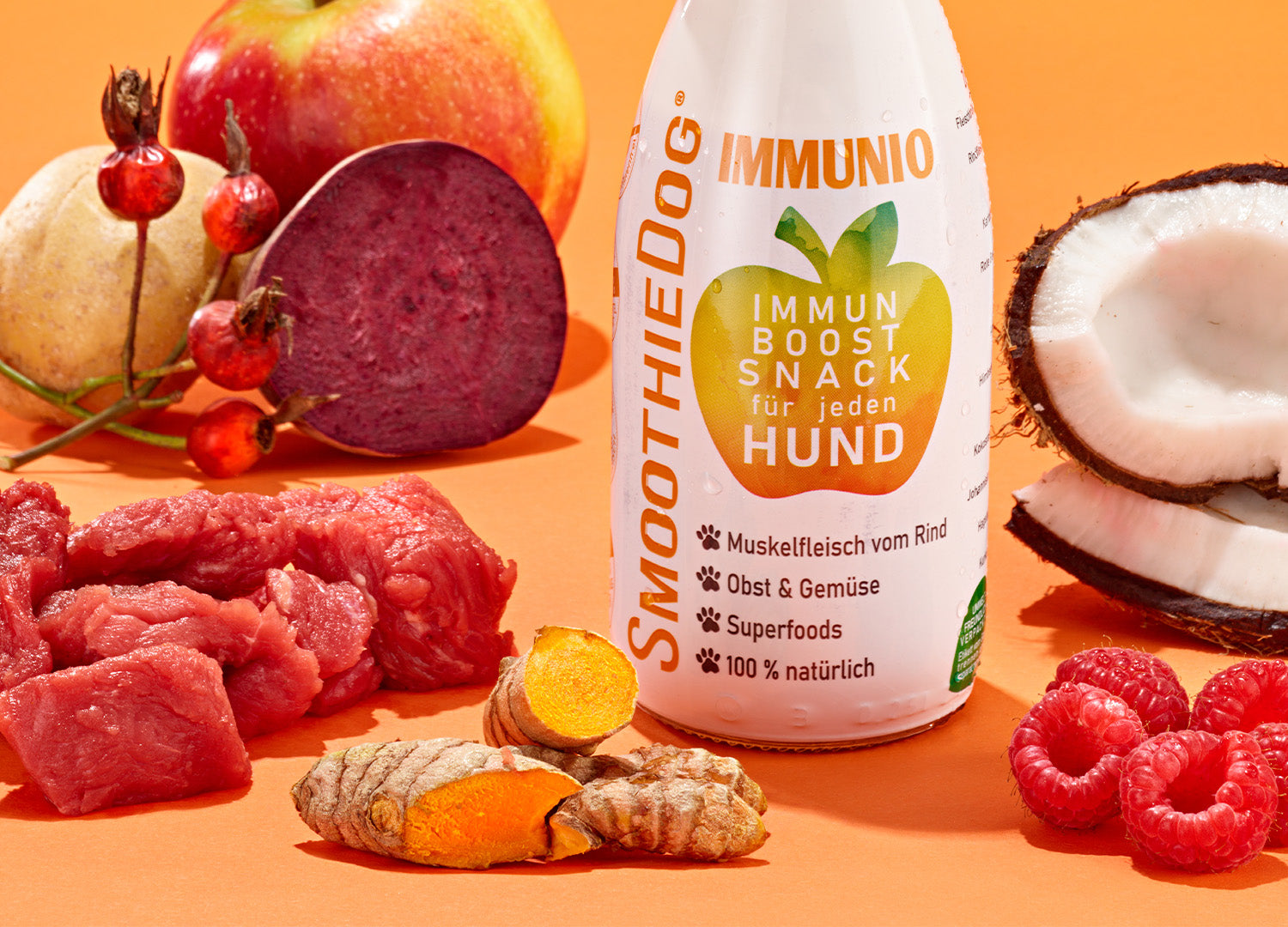 Zeigt die Hundesmoothie Sorte Immunio (Rind) vor einem orangenen Hintergrund. Daneben sind die Zutaten verteilt.